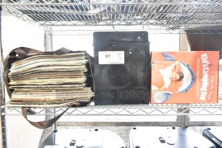 Husky black metal toolbox, stack of records, and kid's camping tent in a shark design on a metal shelf, auction lot label 61.