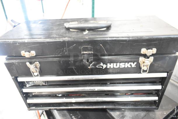 Husky black metal toolbox with three drawers, visible scratches, metal latches, and handle; includes tools, records, and tent.