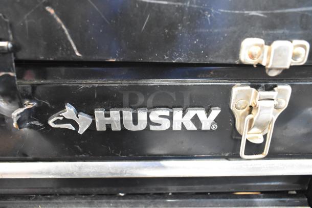 Husky black metal toolbox with visible logo and metal latches, part of an auction lot with tools, records, and a tent.
