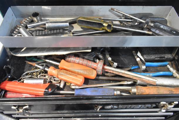 Husky black metal toolbox filled with assorted hand tools and accessories, including screwdrivers and pliers. Slightly worn condition.