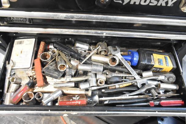Husky black metal toolbox filled with various tools including wrenches, sockets, and screwdrivers; appears used.