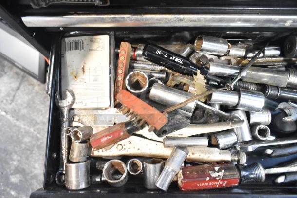 Husky black metal toolbox with assorted tools including wrenches, sockets, and screwdrivers. Signs of wear visible.