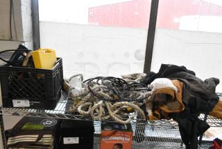 A collection of items including Ryobi saw, ropes, Berne Apparel and Carhartt overalls on a shelf. Items appear used.