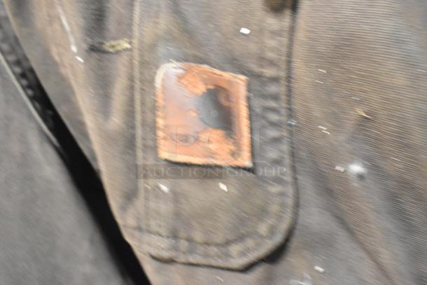 Close-up of worn Carhartt overalls showing a frayed leather label on dark fabric, part of a tiered auction lot.
