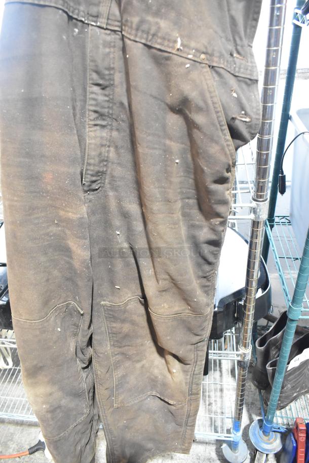 Dirty overalls hanging on a metal rack. Signs of wear and staining indicate usage but may still be functional for work.