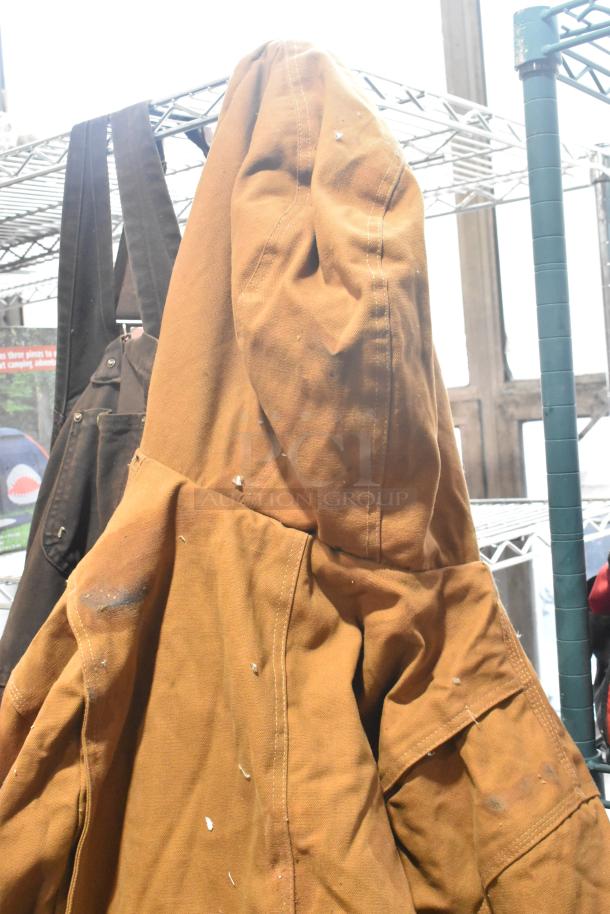 Brown Carhartt overalls, used condition, with visible wear, hanging on a metal rack.