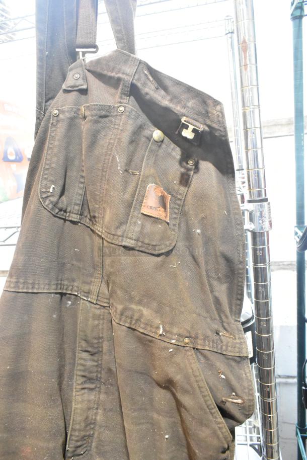 Worn Carhartt overalls with minor stains, visible logo patch. Durable construction, suitable for workwear enthusiasts.