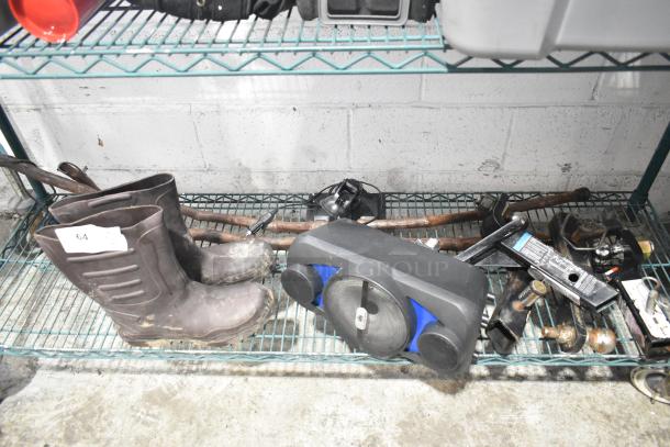 Tiered lot including muddy boots, a black and blue speaker, hitch components, and various tools on a metal shelf.