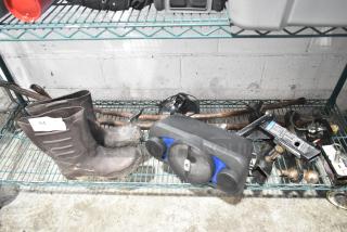Tiered lot including muddy boots, a black and blue speaker, hitch components, and various tools on a metal shelf.