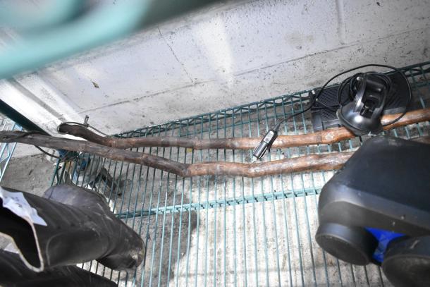 Assorted items including a pair of black boots, electronic speaker, metal hitch, and wiring on a wire shelf. Items show signs of wear.
