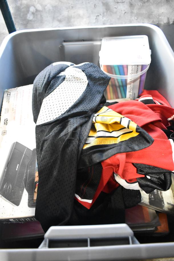 Auction lot containing a portable DVD player, DVDs, assorted clothing, colorful markers, and tools in a plastic bin.