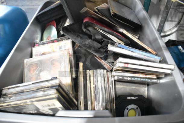 Box of various items including DVDs, portable DVD player, markers, tools, and a Defiant flashlight. Some CDs have visible cases.