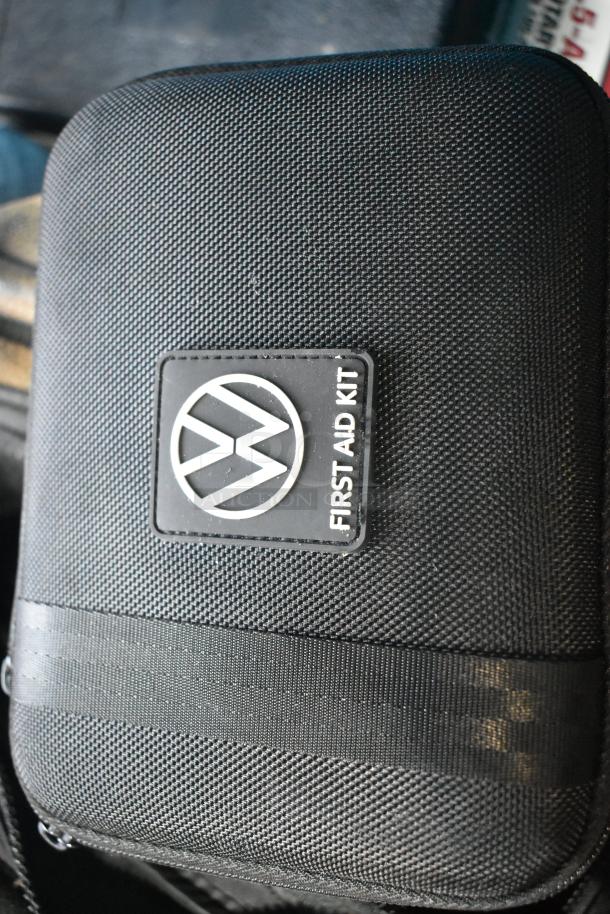 VW-branded first aid kit in a black case, textured surface, featuring logo and label. Part of a mixed item auction lot.