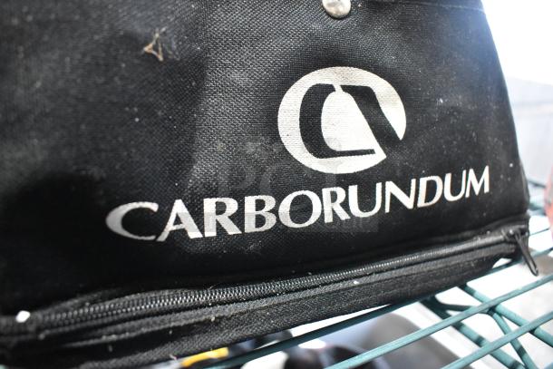 Carborundum tool bag, black with logo, shows some wear. Contains tools, Permatex gasket maker toy, first aid kit, HWStar LED headlights.