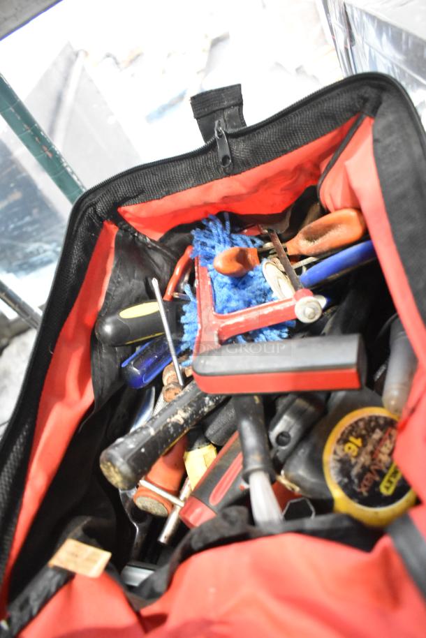 Red tool bag filled with assorted tools, Permatex gasket maker, and first aid kit, showing signs of use.