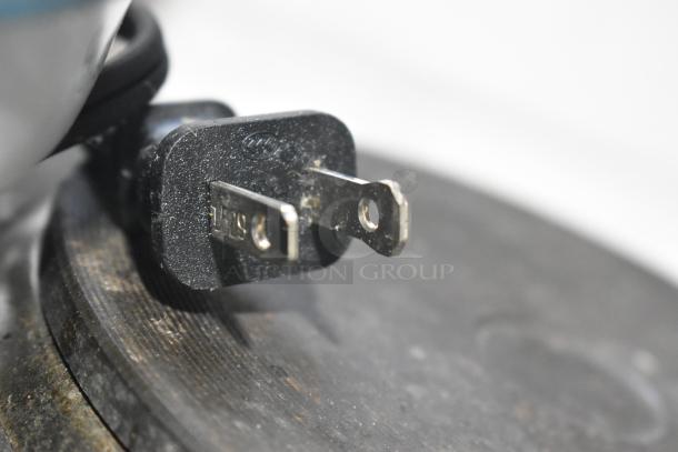Close-up of a two-prong plug attached to an electrical appliance, showing slight wear on the metal prongs.