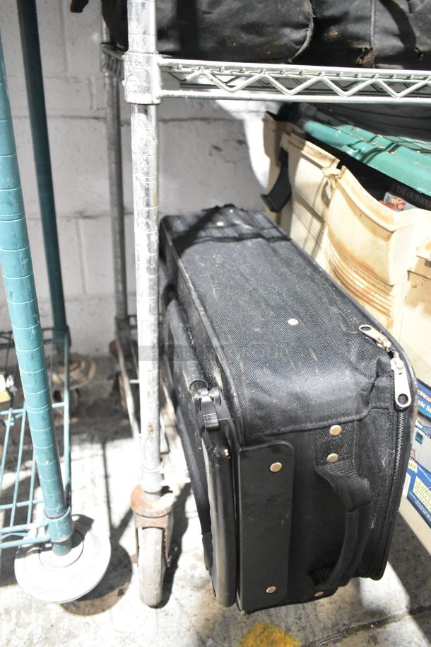 Black luggage on metal shelf, visible wear. Includes poly bins and DVDs. Auction lot with diverse items.