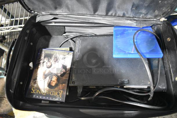 Various items including a DVD of "The Lord of the Rings," PS4 console, and cables inside a black luggage case.