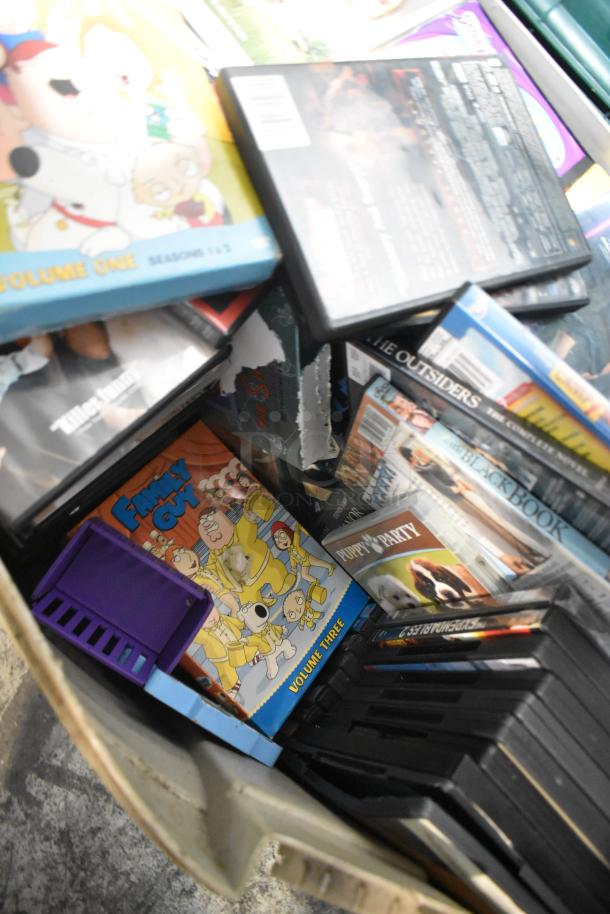 Tier lot of DVDs including "Family Guy" and "Puppy Party," assorted media cases, and visible luggage in fair condition.