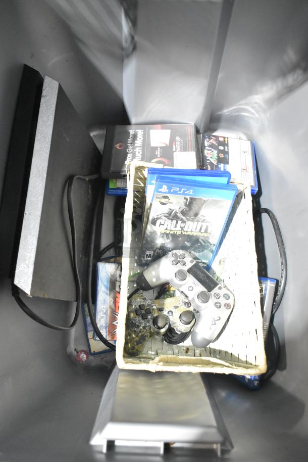 PS4 console with controllers and game cases, including "Call of Duty: Infinite Warfare," inside a poly bin; mixed condition.