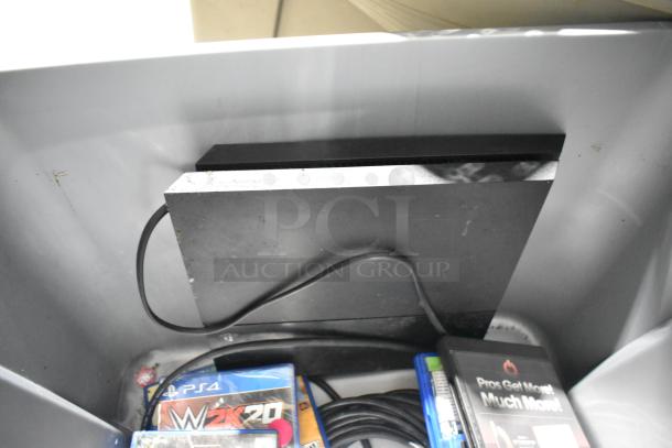 Assorted auction lot with a PS4, DVDs, and cables in a storage bin. Items appear used. Includes PS4 WWE 2K20 game.