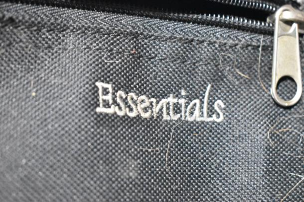 "Essentials" embroidered on black fabric of a luggage item, featuring a silver zipper. Slight wear visible.