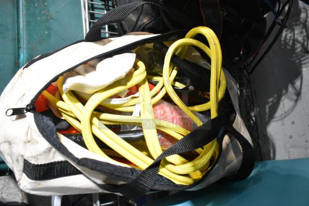 Canvas bag filled with jumper cables, tools, and a rainsuit, showing signs of use. Bag is open with visible contents.