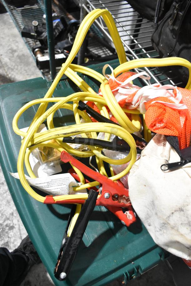 Tier lot of various items including yellow jumper cables and orange rainsuit, on a green surface, tools visible in the background.