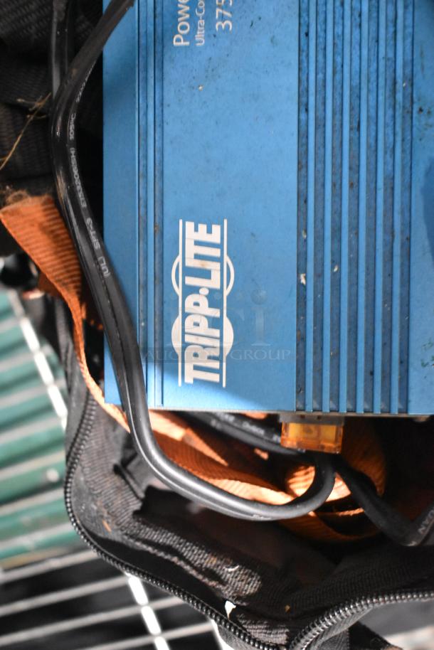 Tripp Lite power inverter on a shelf with cables and a bag; part of a mixed lot including tools and a rainsuit.