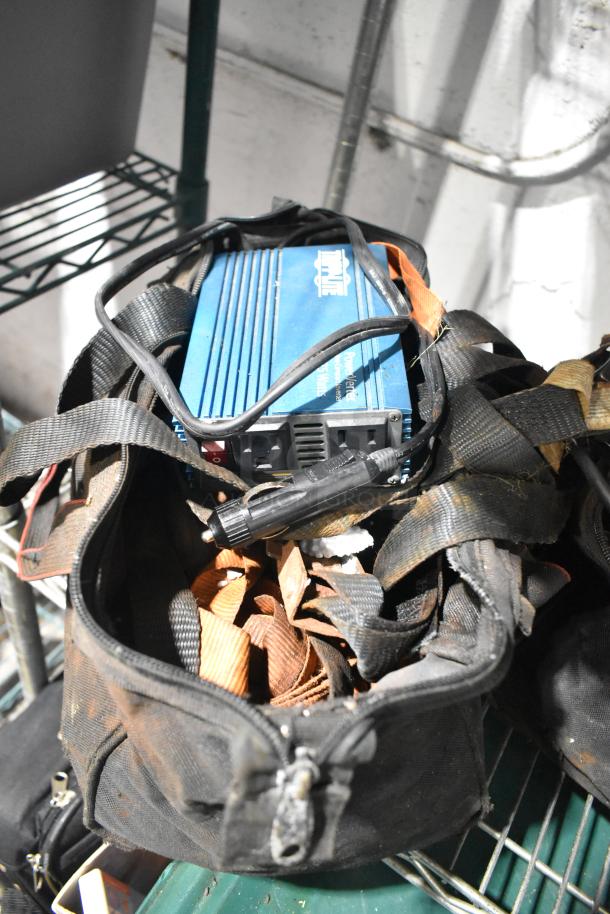Bag containing jumper cables, tools, and a rainsuit. Includes a blue Maxx Power Inverter model PMD500 with visible outlets.