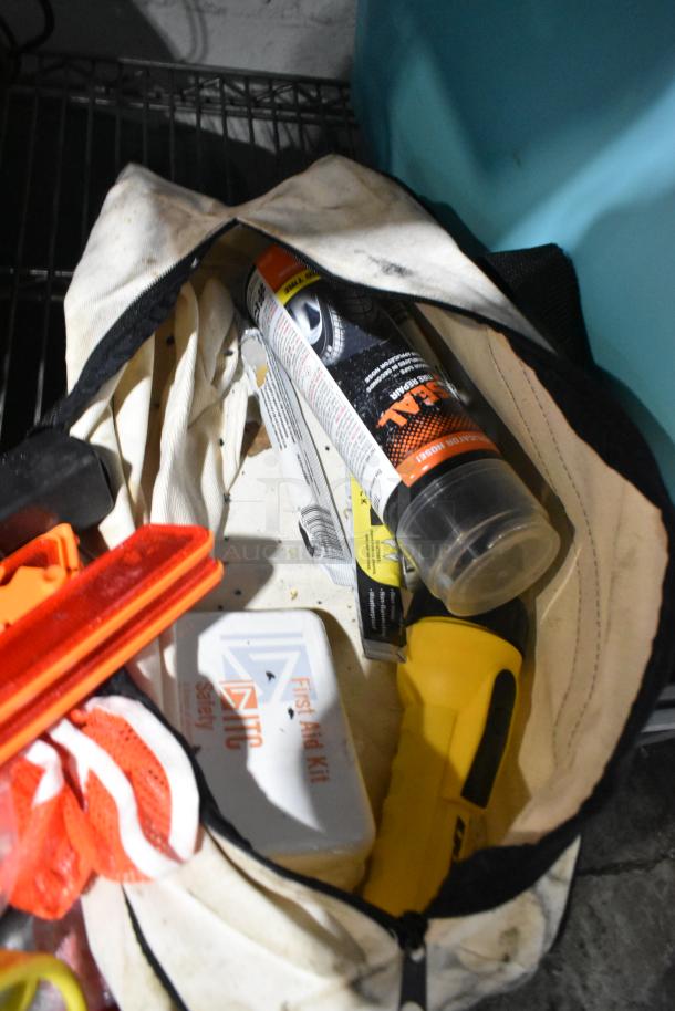 Tiered lot with jumper cables, tools, and a rainsuit in a used tote. Includes a first aid kit and other random items.