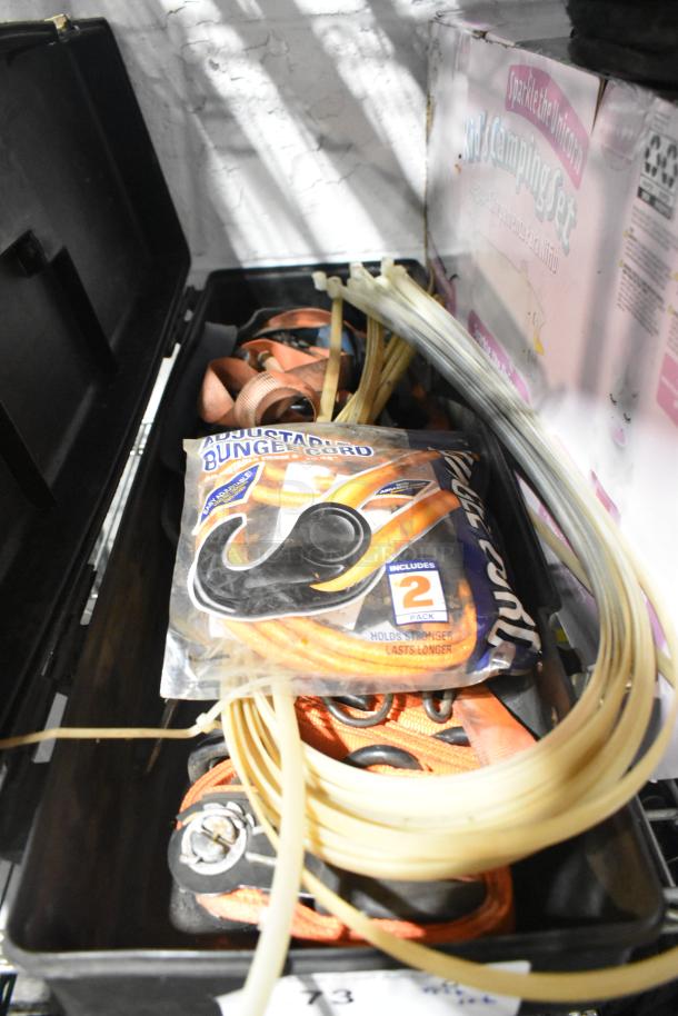 Various items in a storage box, including adjustable bungee cords, plastic tubing, and a unicorn camping set visible in the background.