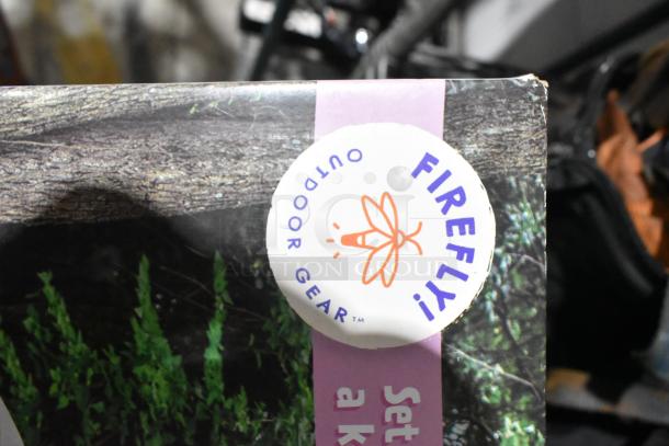 Firefly Outdoor Gear label on a tree-textured surface, part of a mixed auction lot including CDs, a unicorn tent, Jeep bag, and Westward power source.