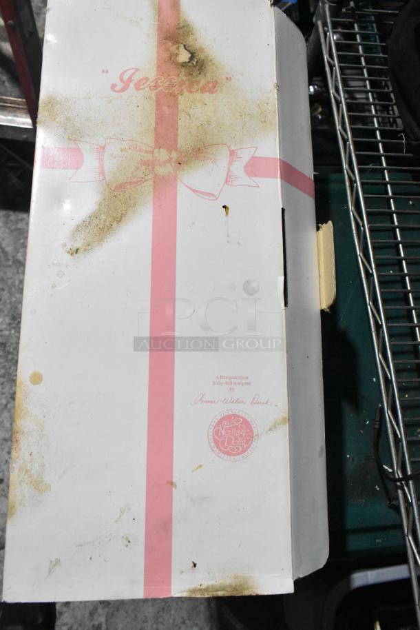 "Jessica" porcelain doll box, visibly stained, by Heritage Dolls. Decorated with pink ribbon design, closed packaging.
