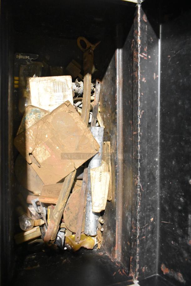 Mixed toolbox contents with rusty tools, metal parts, and a Philips battery pack. Contains signs of wear.