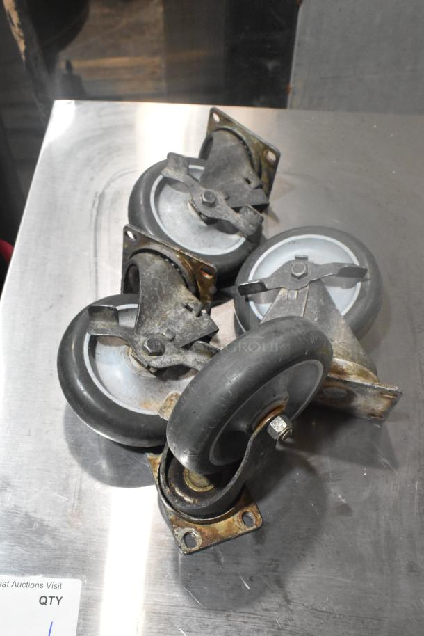 Lot of 4 metal swivel casters with rubber wheels, used condition, resting on a metallic surface.