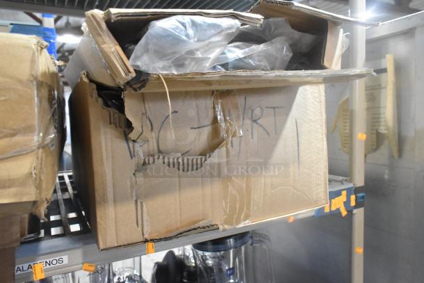 Cardboard box labeled "PC - RT" and "SCRATCH AND DENT" on shelf, slightly damaged, containing shrink-wrapped items.