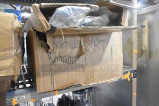 Cardboard box labeled "PC - RT" and "SCRATCH AND DENT" on shelf, slightly damaged, containing shrink-wrapped items.