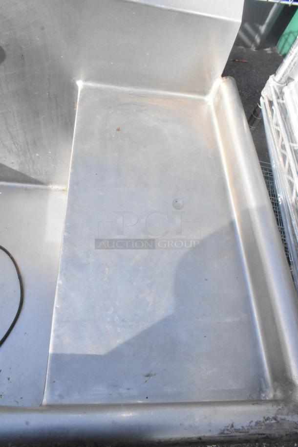 Stainless steel 3-bay sink with right-side drain board, two installed faucets, visible wear, suitable for commercial use.