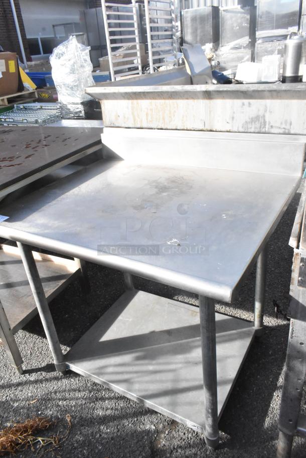 Stainless steel table with back splash, metal under shelf, minor wear, suitable for commercial use, sturdy construction.