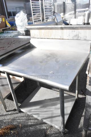 Stainless steel table with back splash, metal under shelf, minor wear, suitable for commercial use, sturdy construction.