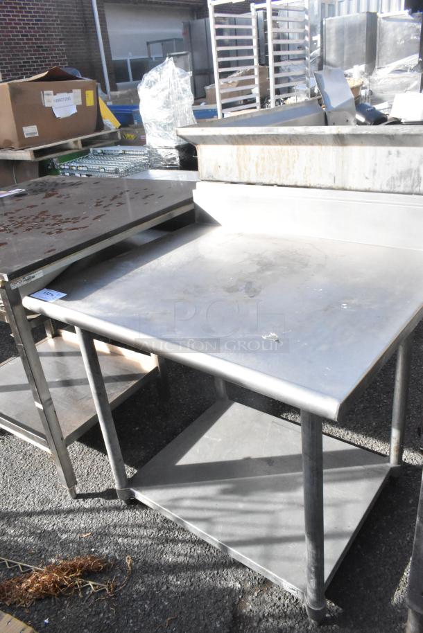 Stainless steel table with back splash, features a sturdy metal under shelf, showing signs of wear. Perfect for kitchen use.