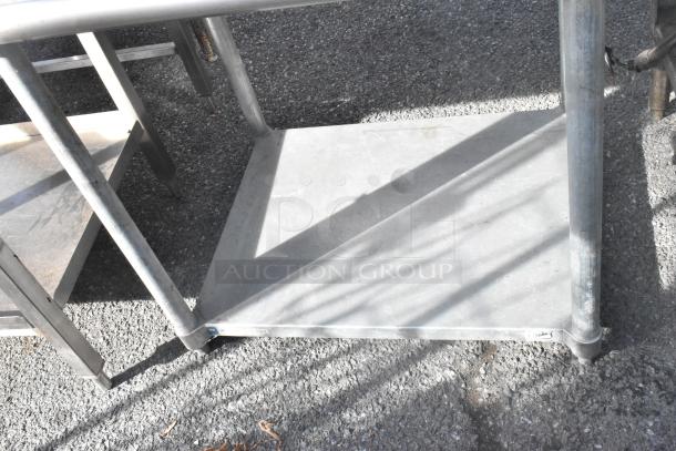 Stainless steel table with back splash, metal under shelf, sturdy frame. Visible signs of use, ideal for industrial settings.