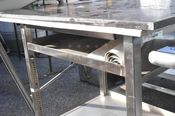 Stainless steel metal table with adjustable under shelf, label marked "SPG", in used condition with slight surface wear.