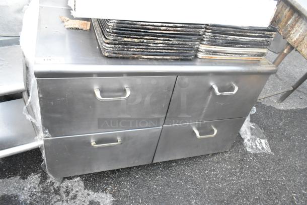 Stainless steel 4-drawer counter in used condition, featuring sturdy handles. Ideal for kitchen or restaurant use.