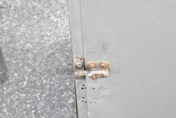 Metal portable enclosed pan rack with visible rusty latch detail. Hinged door with ventilation holes. Used condition.