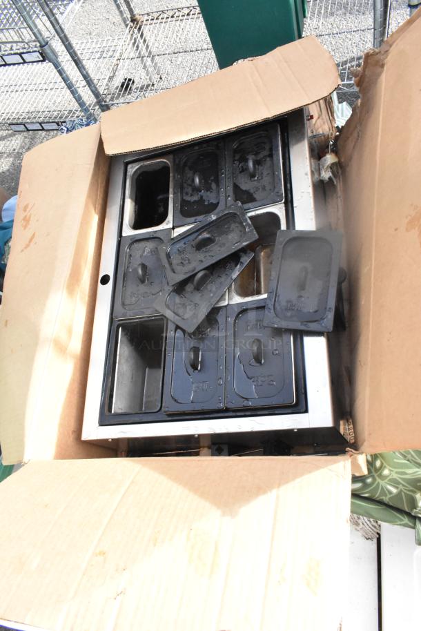 Cardboard box containing metal trays with black lids, showing signs of wear. Part of a 14-item auction lot.