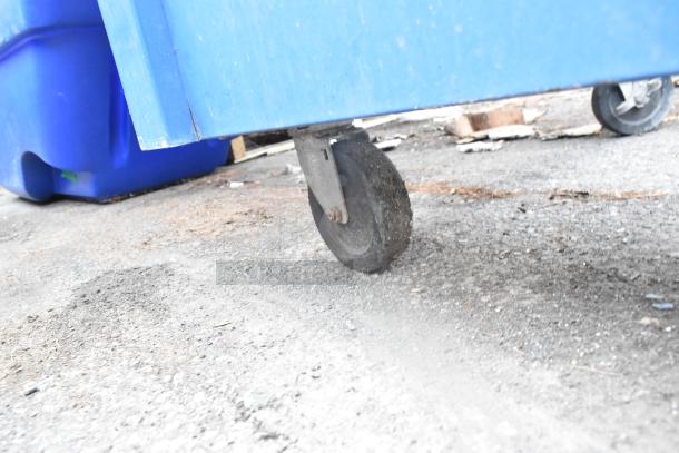 Blue bin on casters, shown on a rough outdoor surface. Features sturdy wheels for mobility. Slight wear visible.