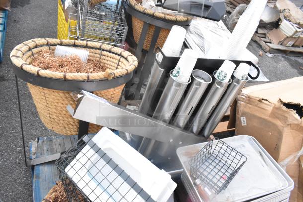 Pallet lot with wicker basket, metal baking pans, stainless cup dispensers, and wire baskets. Used condition, mixed items.