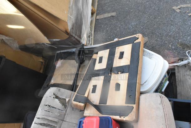 Alt text: Assorted items including damaged seat cushion and a wooden board with black tape, placed on outdoor ground.